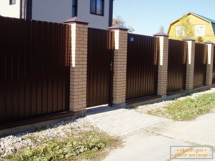 La valla modular es de color marrón oscuro con acabado de ladrillo, un clásico del género, si hablamos del diseño de áreas suburbanas.