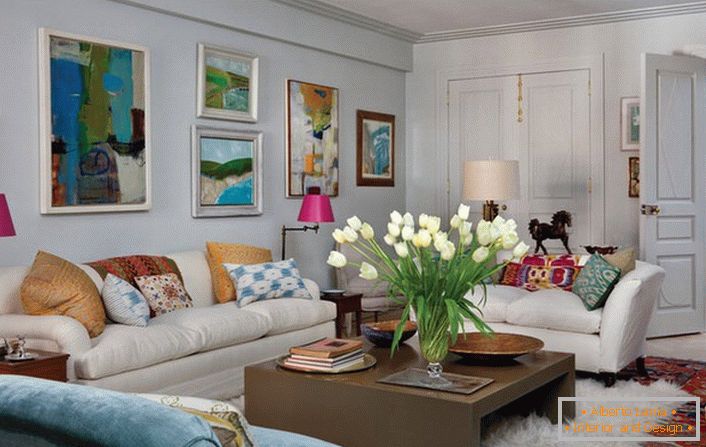 Sala de estar universal en estilo ecléctico. Una habitación acogedora hace un montón de almohadas y pinturas abstractas y brillantes que adornan la pared sobre el sofá.