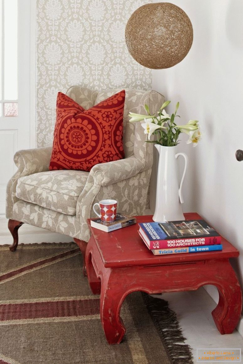 Rincón de lectura; mesa de opio y sillón pálido con cojines de dispersión estampados contra la pared empapelada