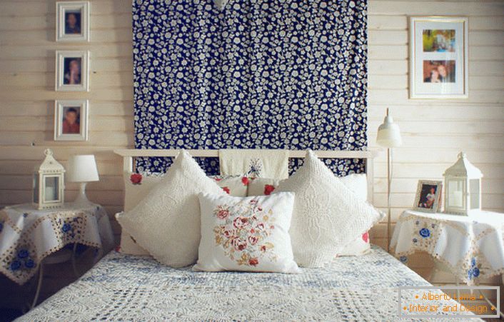 De acuerdo con el estilo rústico, la cama está decorada con varias almohadas con bordados rojos en contraste. Las mesitas de noche están cubiertas con un mantel con delicadas flores azules.