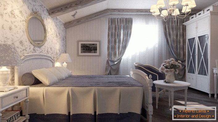 El dormitorio en estilo country está hecho en tonos azules apagados. La pared en la cabecera de la cama está cubierta con papel tapiz con motivos florales.