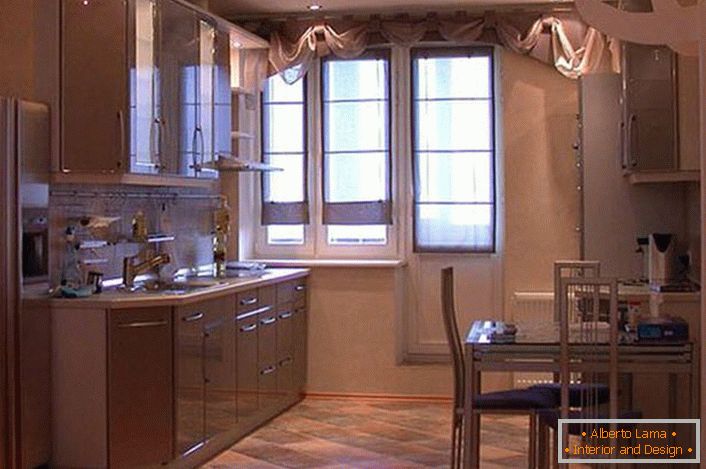 Un amplio juego de cocina con armarios colgantes en tonos beige claro se ve atractivo y exquisito. En lugar de una despensa, el diseñador hizo un nicho, donde por conveniencia se colocó un refrigerador.