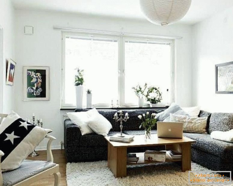 Una pequeña sala de estar en blanco con un sofá de esquina oscuro y una ventana