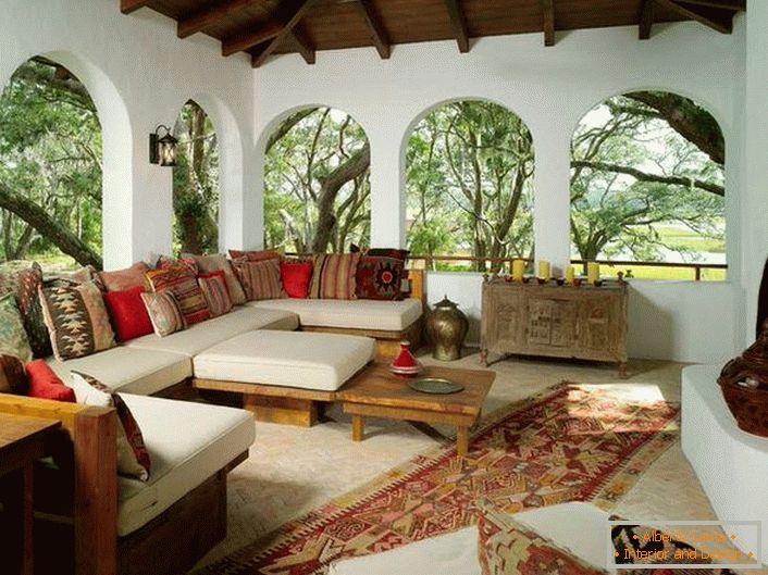 La terraza de la casa de campo está decorada de acuerdo con el estilo mediterráneo. Una característica interesante es la decoración con muchos cojines coloridos.