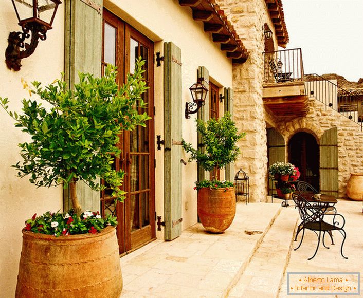 El patio в средиземноморском стиле украшают горшки с живыми растениями. Привлекательный дизайн, мебель с витиеватыми спинками, керамические горшки создают уютную, расслабляющую атмосферу. 