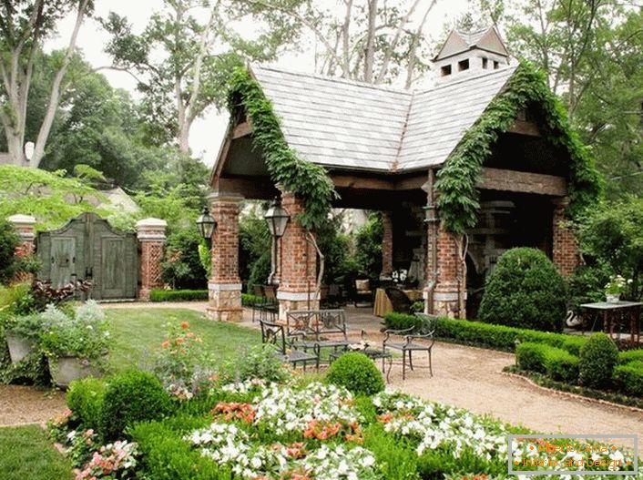 La elegante simplicidad de una glorieta abierta en el estilo de un chalet se ve orgánicamente en un jardín lujoso y acogedor. 