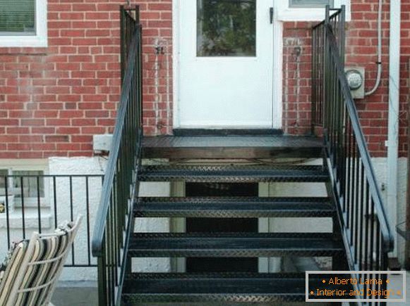Un pequeño porche de metal con una escalera a la casa de ladrillo