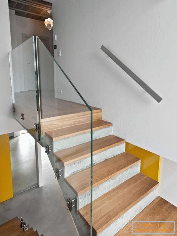 Escalera de hormigón con escalones de madera y barandilla de vidrio en una casa privada