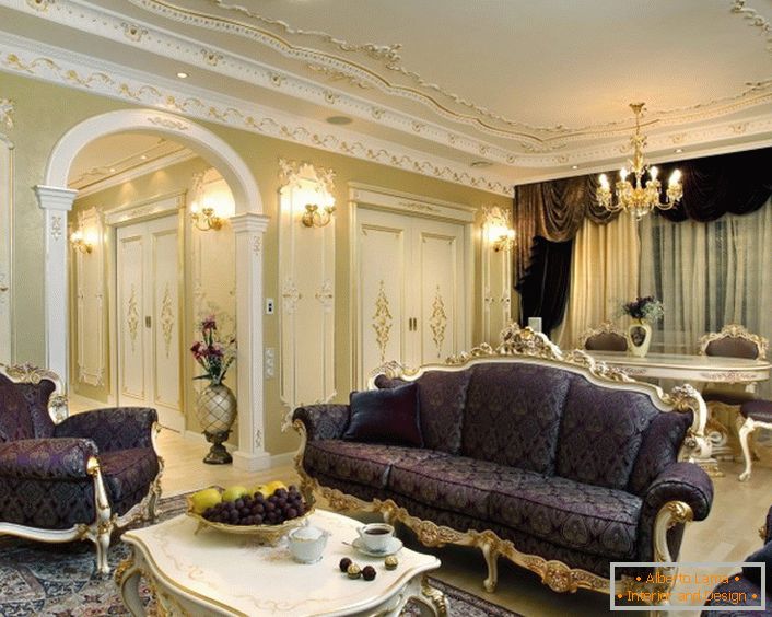 Un ejemplo de una combinación competente de colores en la decoración en el estilo barroco. Los muebles de tapicería, los lambrequines y la alfombra, de color lila, se combinan incluso con uvas en la mesa y flores. Intención de diseño delgado.