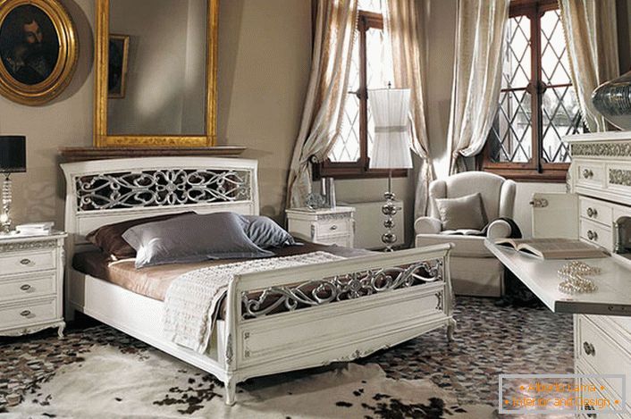 Se observa el requisito básico del estilo barroco. En un amplio dormitorio con techos altos, muebles de madera blanca contrasta con los marcos oscuros de las ventanas.