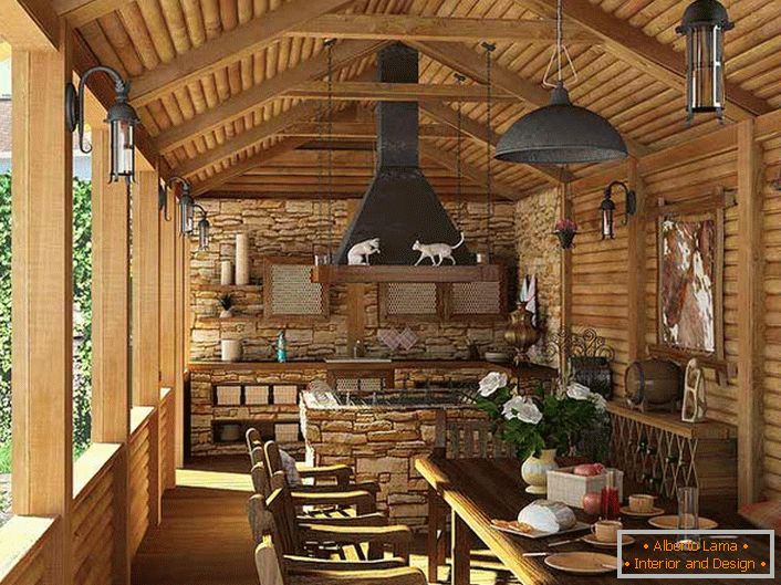 Una pequeña cocina con una barbacoa en la terraza de una casa de campo. El estilo campestre se evidencia, en primer lugar, por la decoración de las paredes y el techo con un marco de madera.