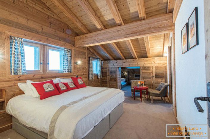 Un amplio dormitorio en el segundo piso de una casa de campo de una casa de troncos de madera. В соответствии со стилем кантри искусственный свет в комнате приглушен. 