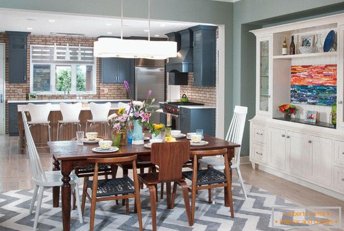 Una gran cocina de estilo ecléctico se divide en una zona de trabajo y comedor. Los muebles del color blanco se combinan con los elementos del interior del color marrón oscuro.